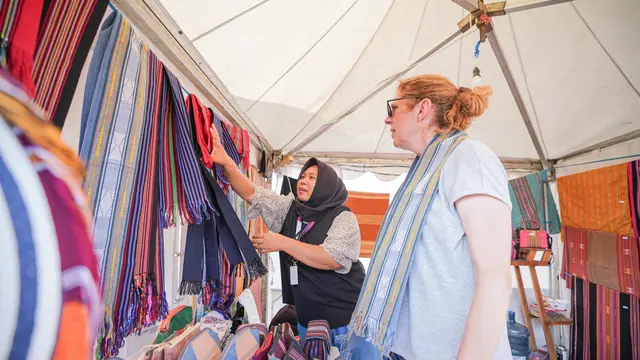 Indonesian MSMEs in global trade showcasing traditional woven fabrics to an international customer at a market stall.