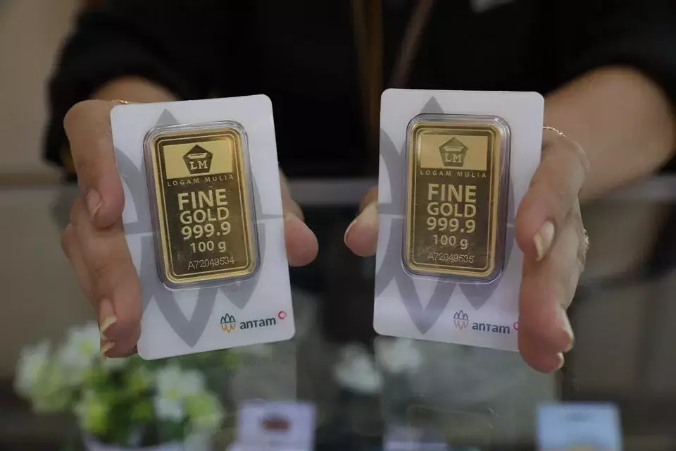 Two hands holding Antam gold bars, 999.9 fine gold, 100 grams each, symbolizing the appeal of gold investment in 2025.