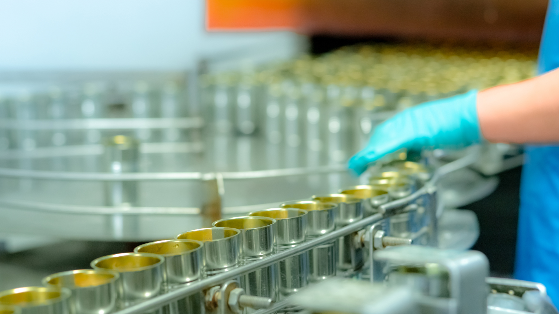 A worker in a food packaging facility inspects tin cans on a conveyor belt, reflecting the growing industrial demand driven by Indonesia tin production.