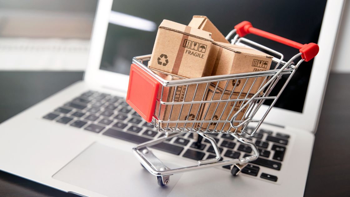 a mini cart carying cardboard boxes on top of a laptop symbolizing online shopping and E-Commerce Tax Policy