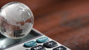 A mini crystal globe on top of a calculator with tax buttons on it symbolizing Indonesia tax incentive shift amid global minimum tax policy