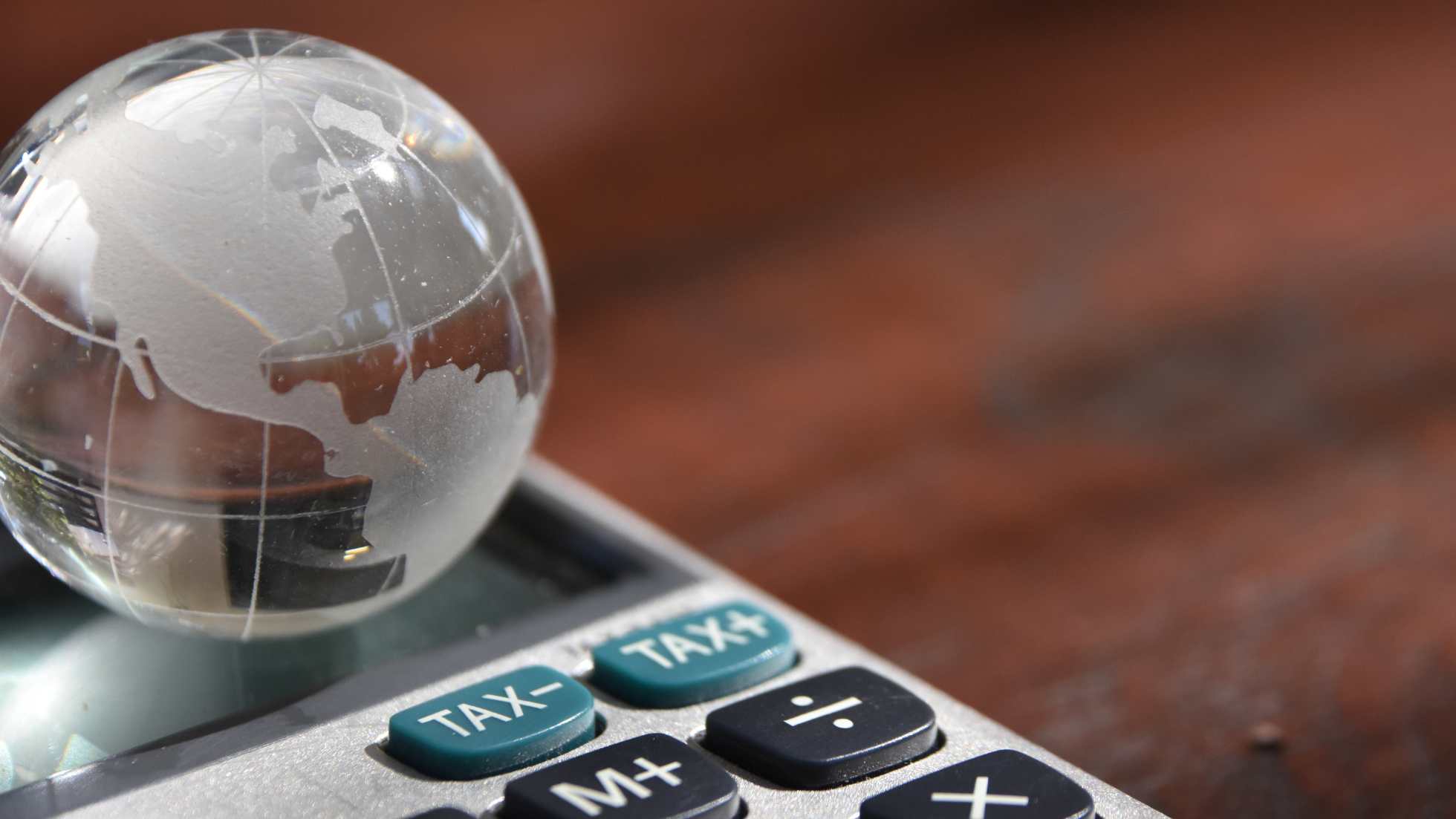 A mini crystal globe on top of a calculator with tax buttons on it symbolizing Indonesia tax incentive shift amid global minimum tax policy