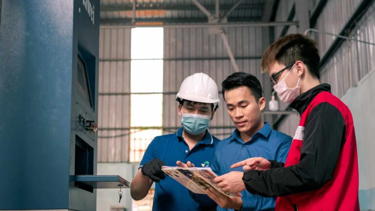Manufacturing investment in Indonesia shown through factory workers collaborating on production plans inside an industrial facility.