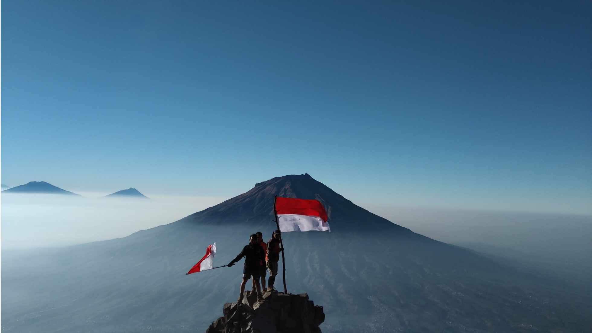 Two people atop a mountain waving the Indonesian flag symbolizing Indonesia's sustainable tourism goals