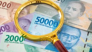 A magnifying glass over Indonesian rupiah banknotes symbolizing close examination of the rupiah redenomination plan.