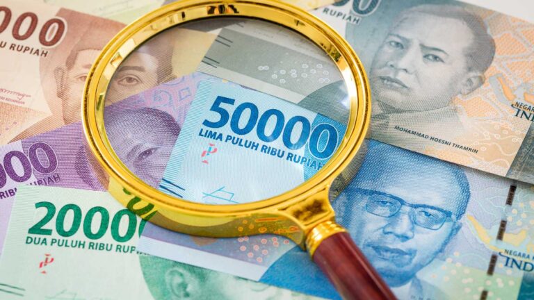 A magnifying glass over Indonesian rupiah banknotes symbolizing close examination of the rupiah redenomination plan.