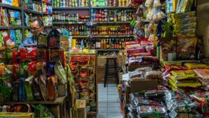 A small Indonesian grocery shop filled with packaged foods, snacks, and imported goods stacked tightly on shelves, illustrating Indonesia import challenges for local MSMEs.