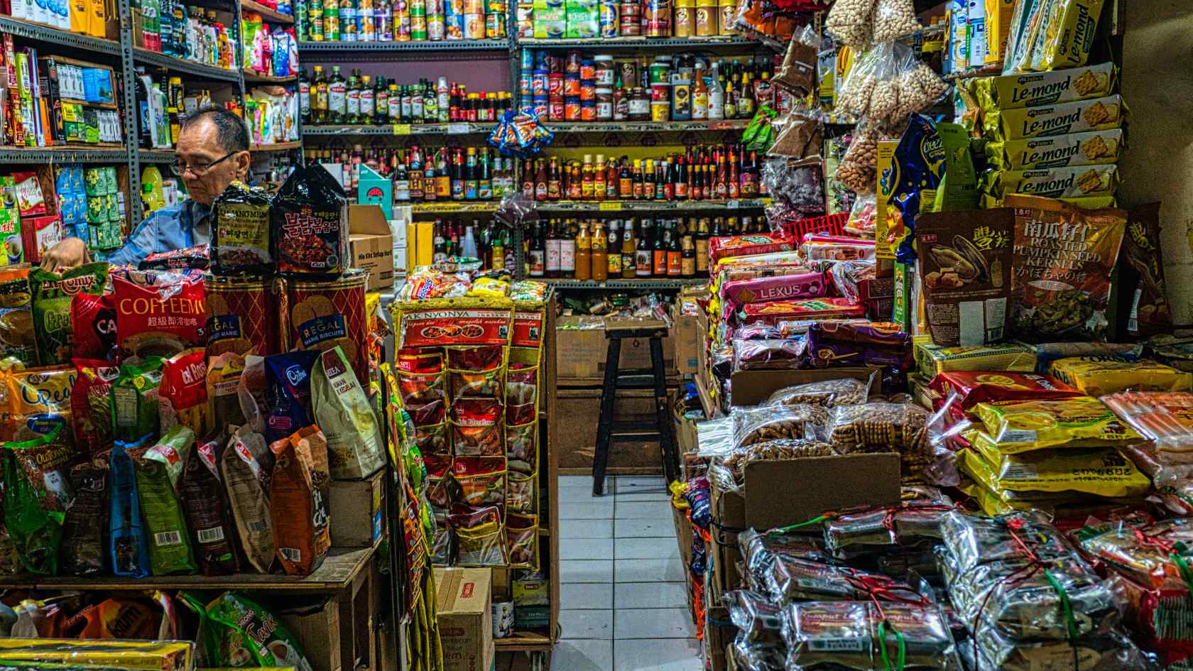 A small Indonesian grocery shop filled with packaged foods, snacks, and imported goods stacked tightly on shelves, illustrating Indonesia import challenges for local MSMEs.